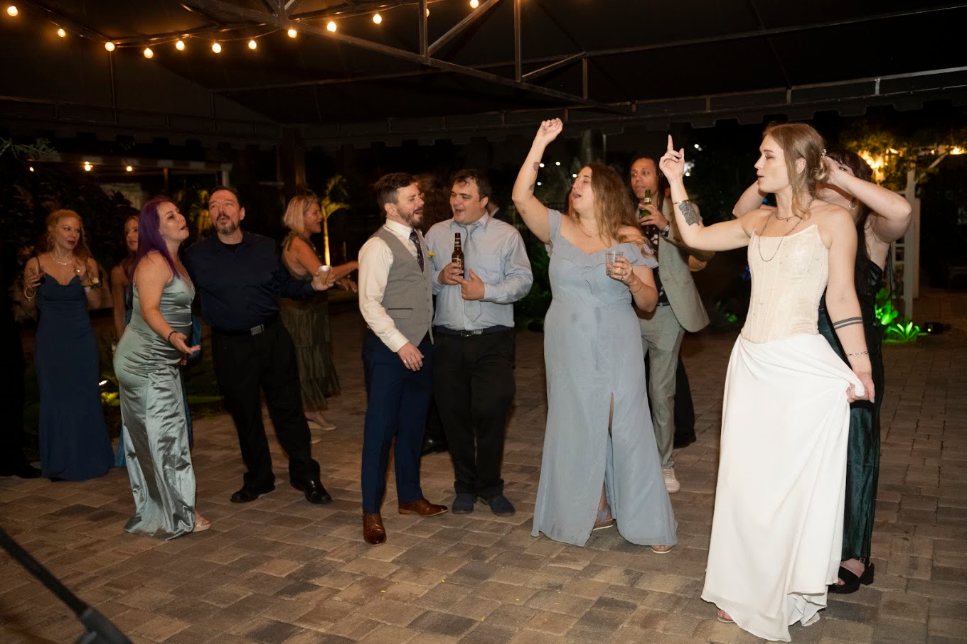 Wedding guests and the bride singing along under string lights